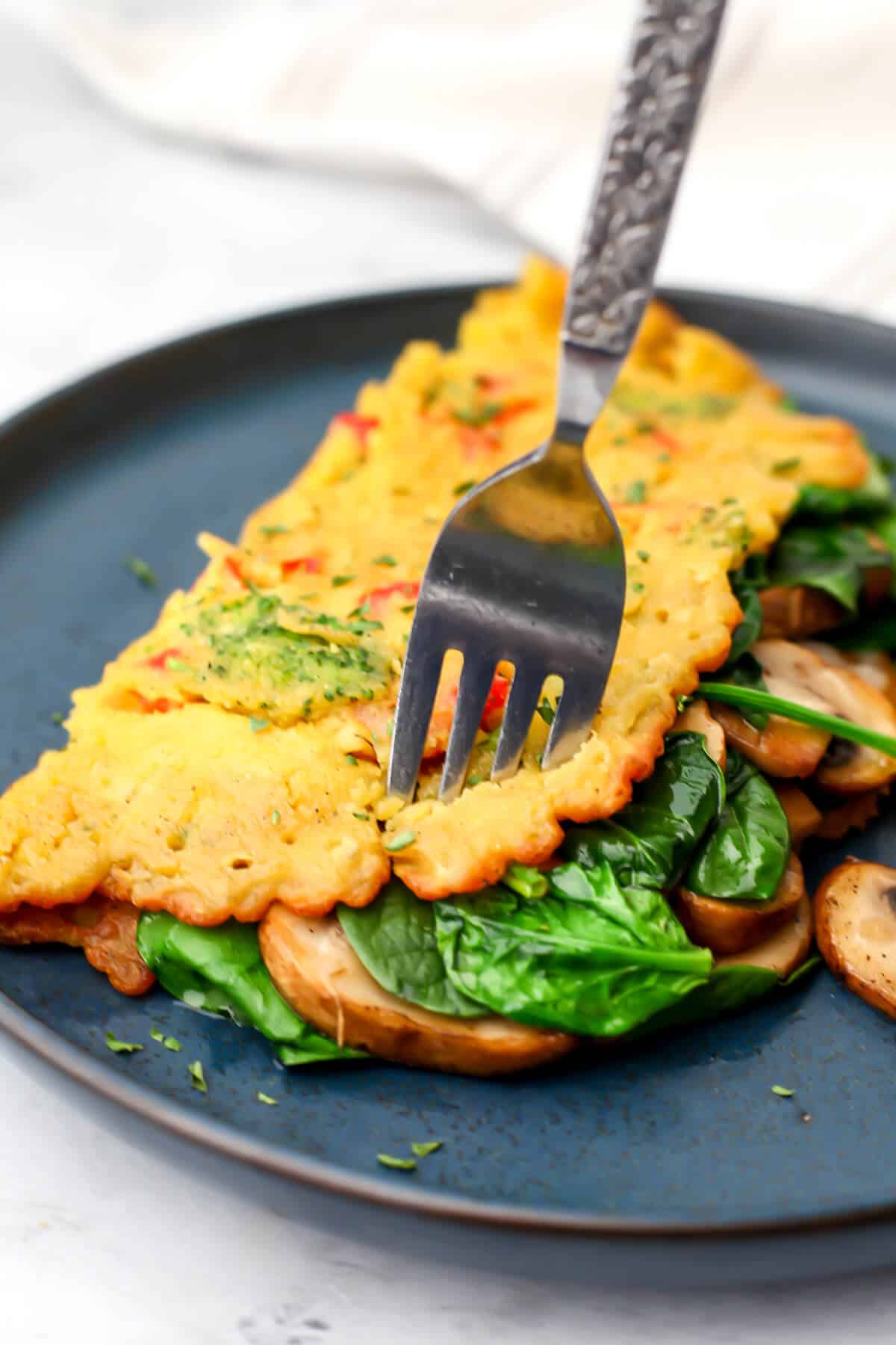 A vegan omelet on a blue plate with a fork sticking in it.