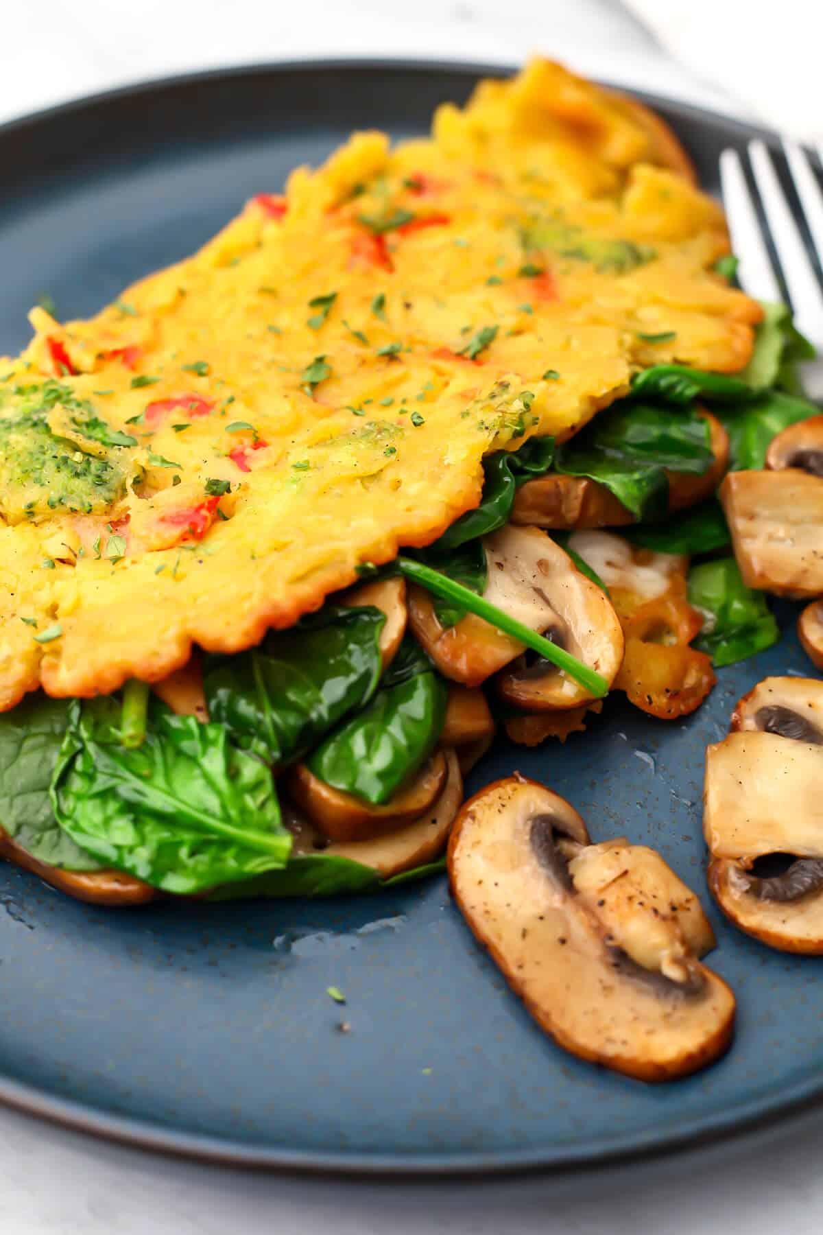 A vegan omelette made with chickpea flour and veggies, filled with vegan cheese, spinach ,and mushrooms.