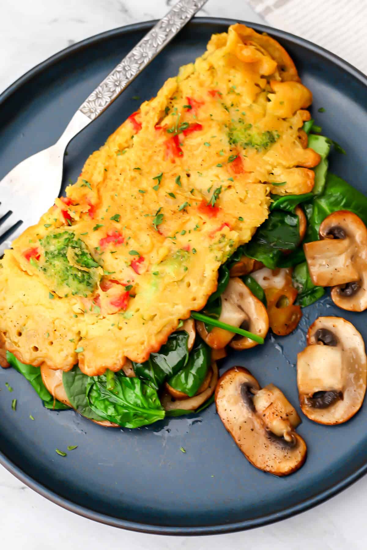 A top view of a vegan omelet made from chickpea flour and veggies on a blue plate.