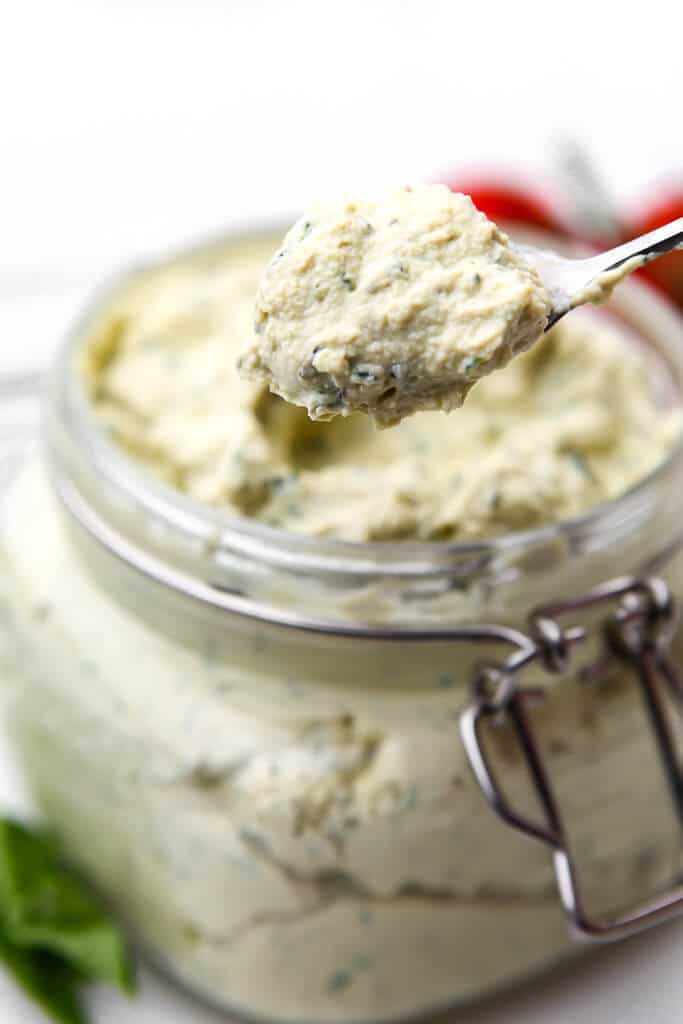 A glass jar filled with vegan ricotta with a spoon scooping some out.