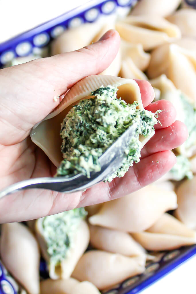 Someone holding a jumbo pasta shell filling it with tofu spinach ricotta cheese.