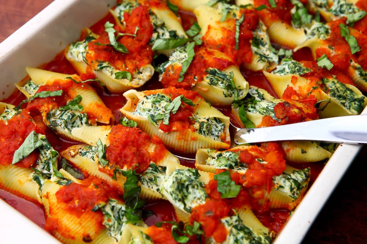 A large baking dish filled with vegan stuffed shells and topped with tomato sauce and fresh basil.