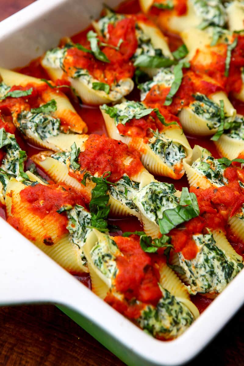A baking dish filled with vegan spinach stuffed shells topped with tomato sauce and fresh basil.