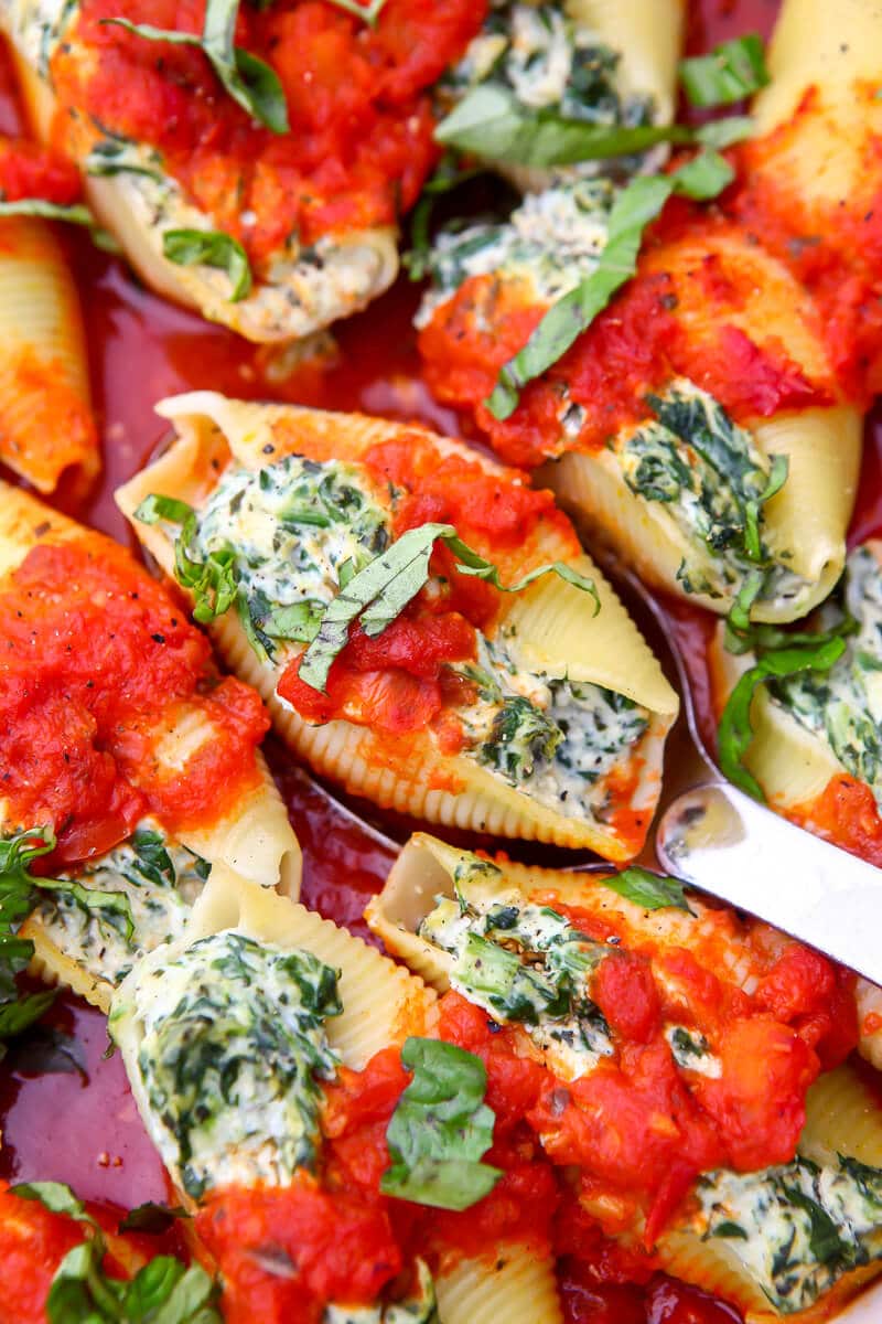 A top view of vegan stuffed shells with a spoon scooping one out of a baking dish.