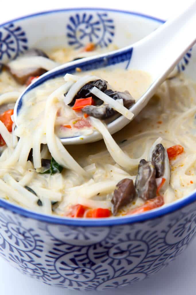 A blue and white bowl of coconut curry soup with rice noodles mushrooms and red bell peppers.
