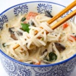 A bowl of coconut curry soup with rice noodles wrapped around chop sticks in a coconut broth.