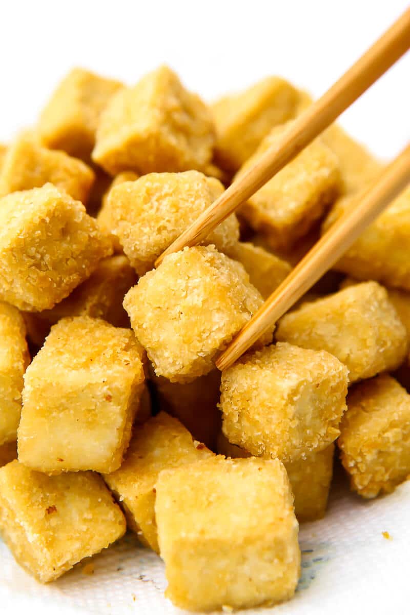 A pile of crispy fried tofu on a paper towel with someone taking a piece with chopsticks.