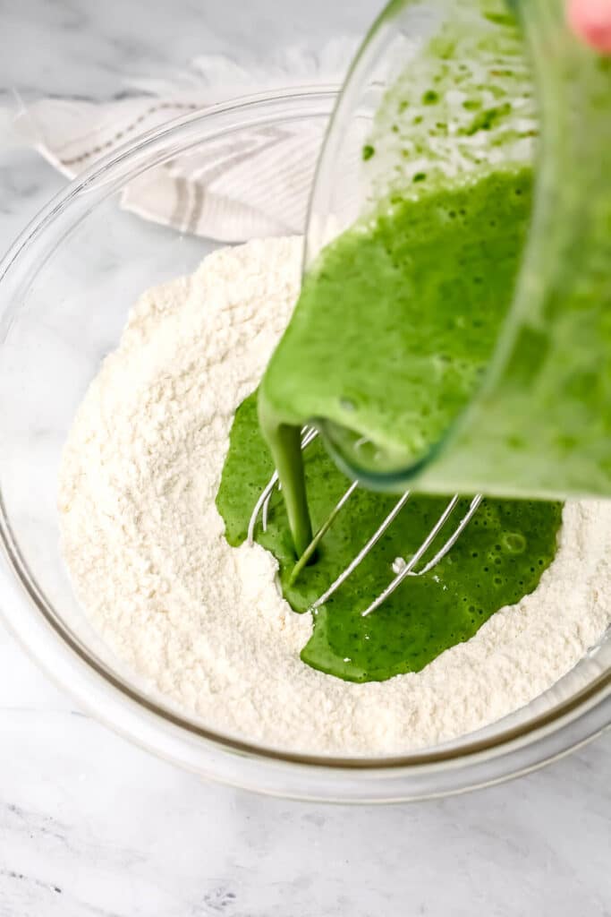 Adding blended spinach to dry ingredients to make spinach blender muffins.