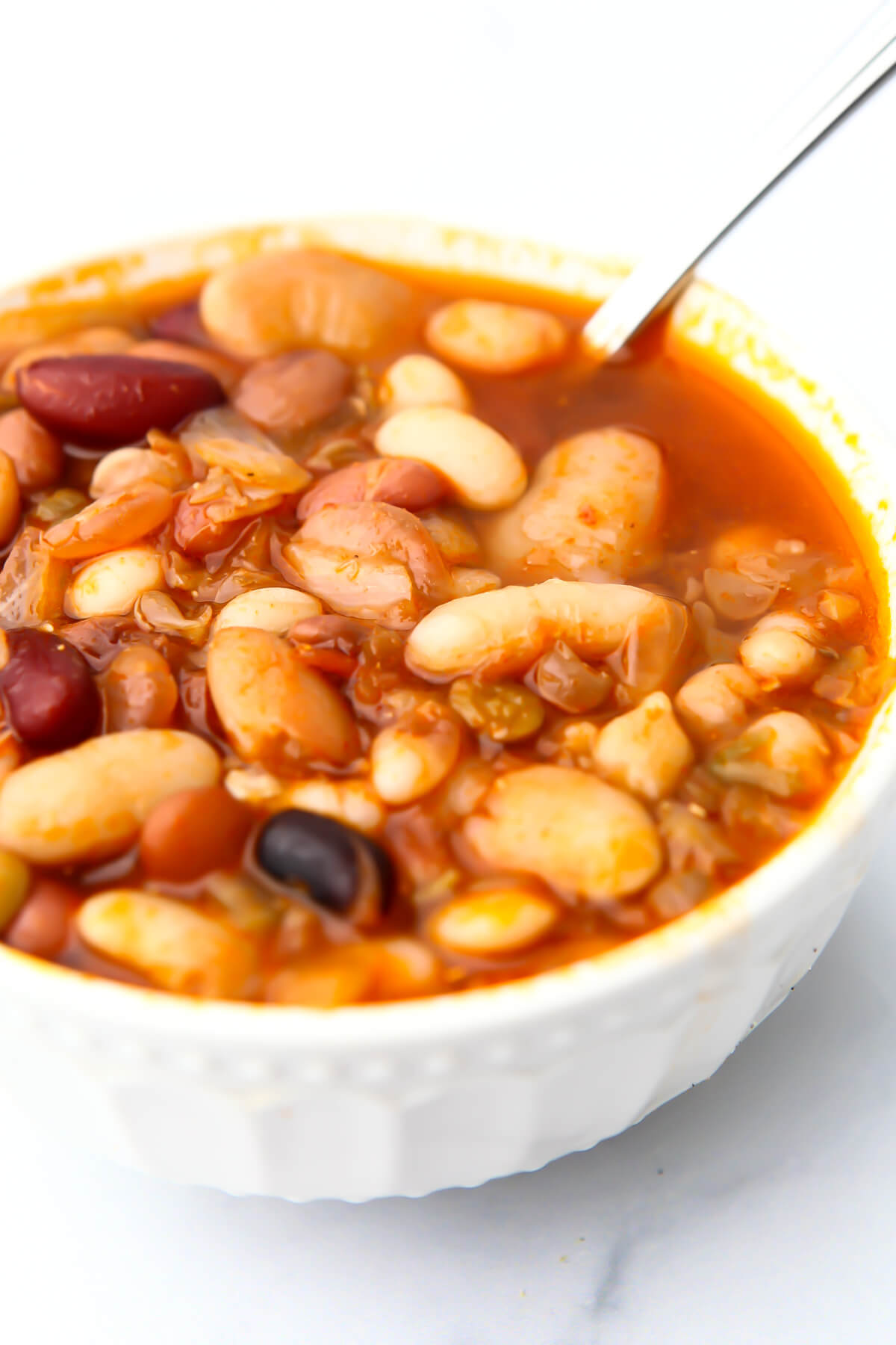 A white bowl filled with vegan 15 bean soup with a spoon in it.