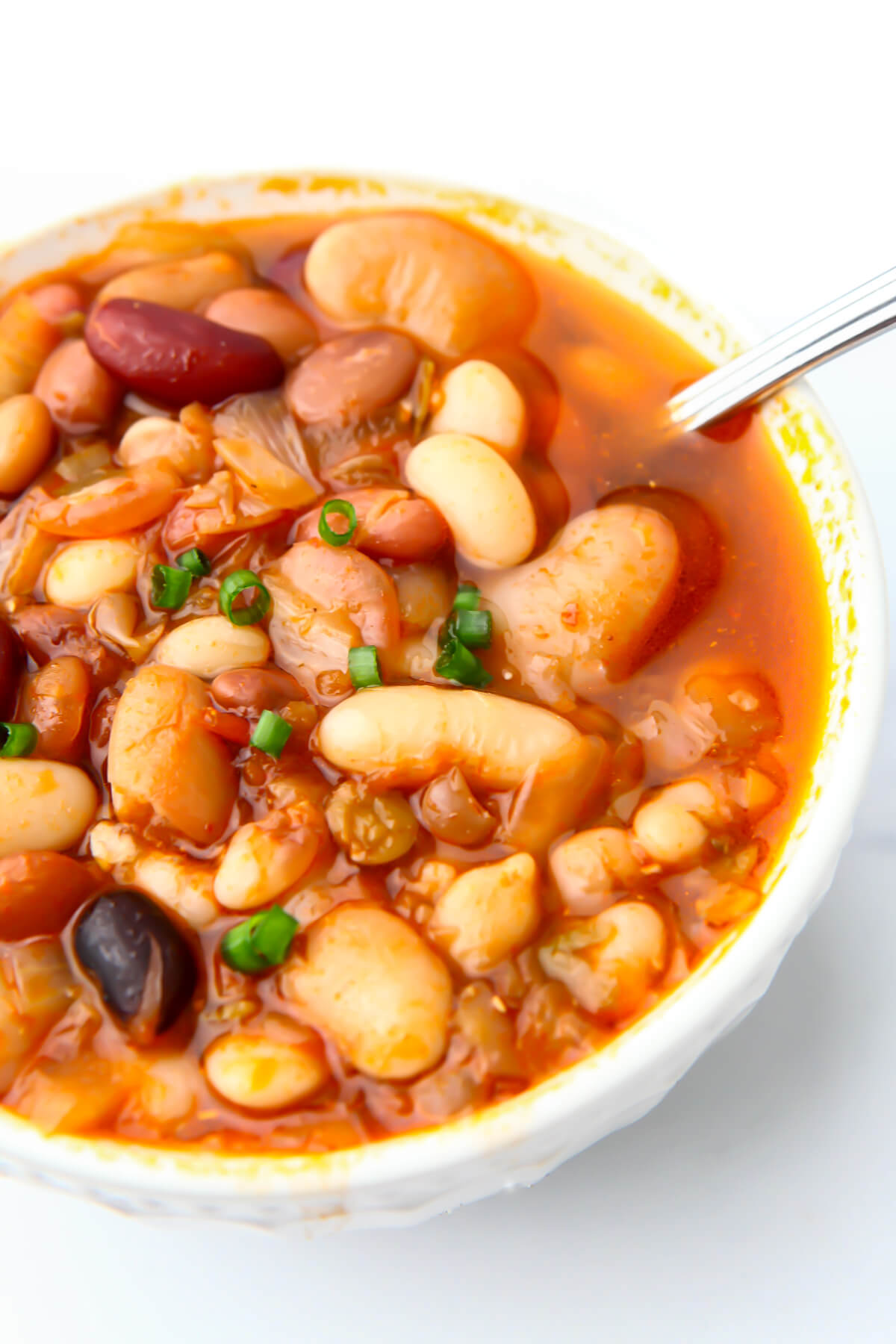 A white bowl filled with vegan bean soup and topped with green onions.
