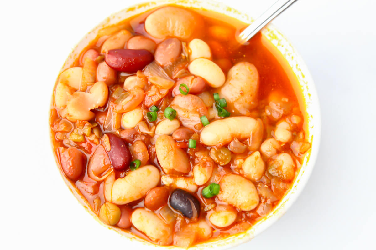 A white bowl filled with vegan 15 bean soup with a spoon in it.