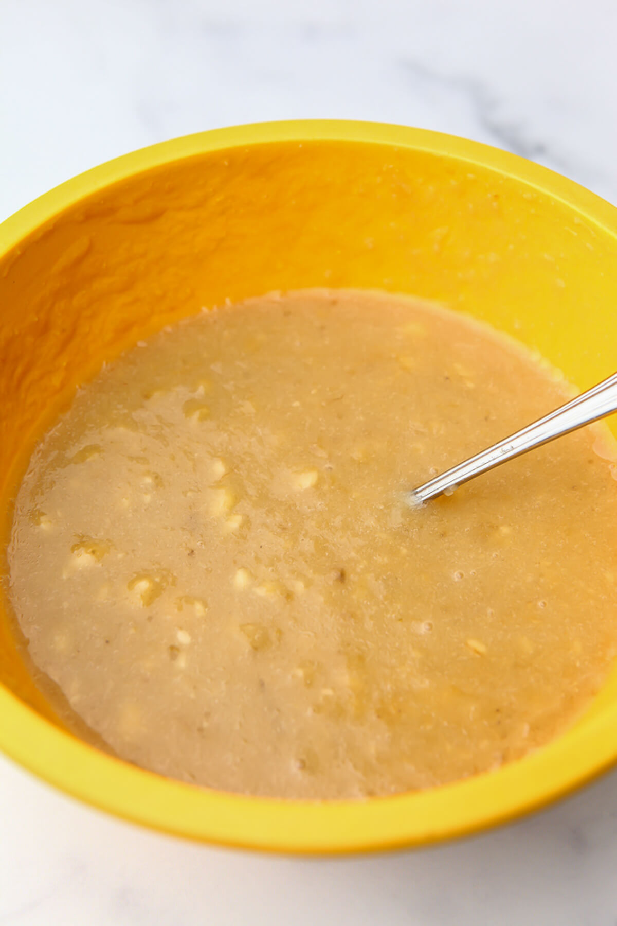 Bananas and sugar mashed together in a yellow bowl.