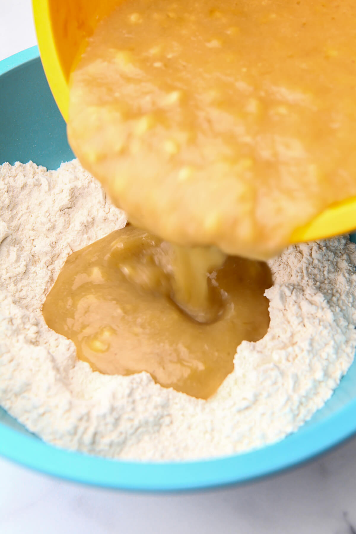 Mashed bananas being poured into the dry ingredients to make vegan banana bread.