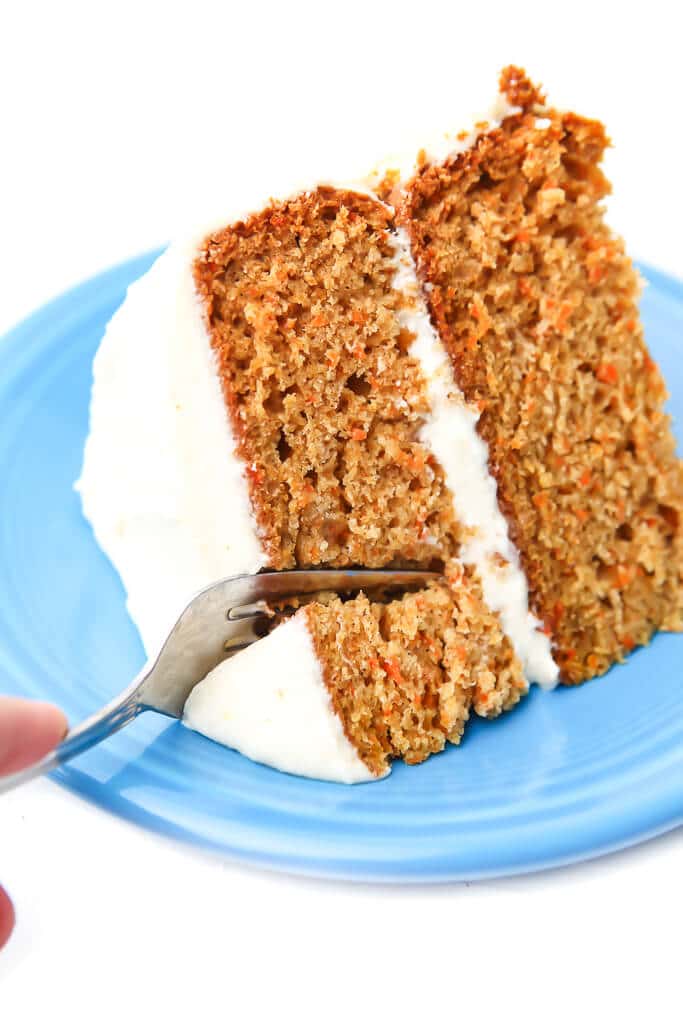 A slice of vegan carrot cake on a blue plate with a fork slicing into it.
