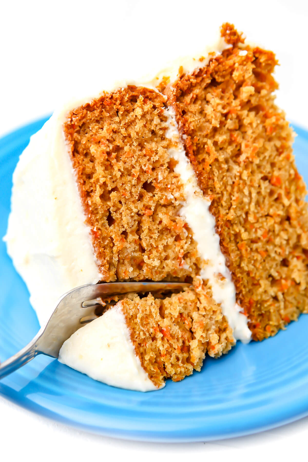 A slice of vegan carrot cake on a blue plate with a fork slicing into it.