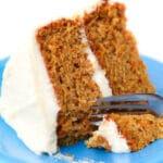 A vegan carrot cake with vegan cream cheese frosting on a blue plate with a fork in it.