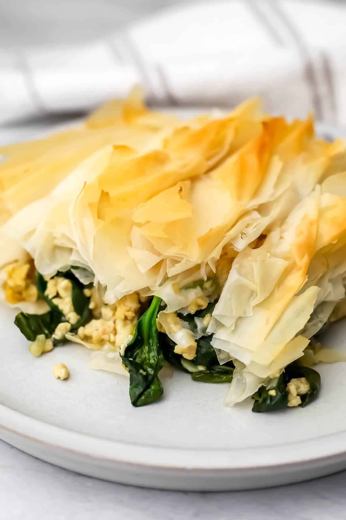 A slice of vegan spanakopita made with tofu with filo on top on a white plate.