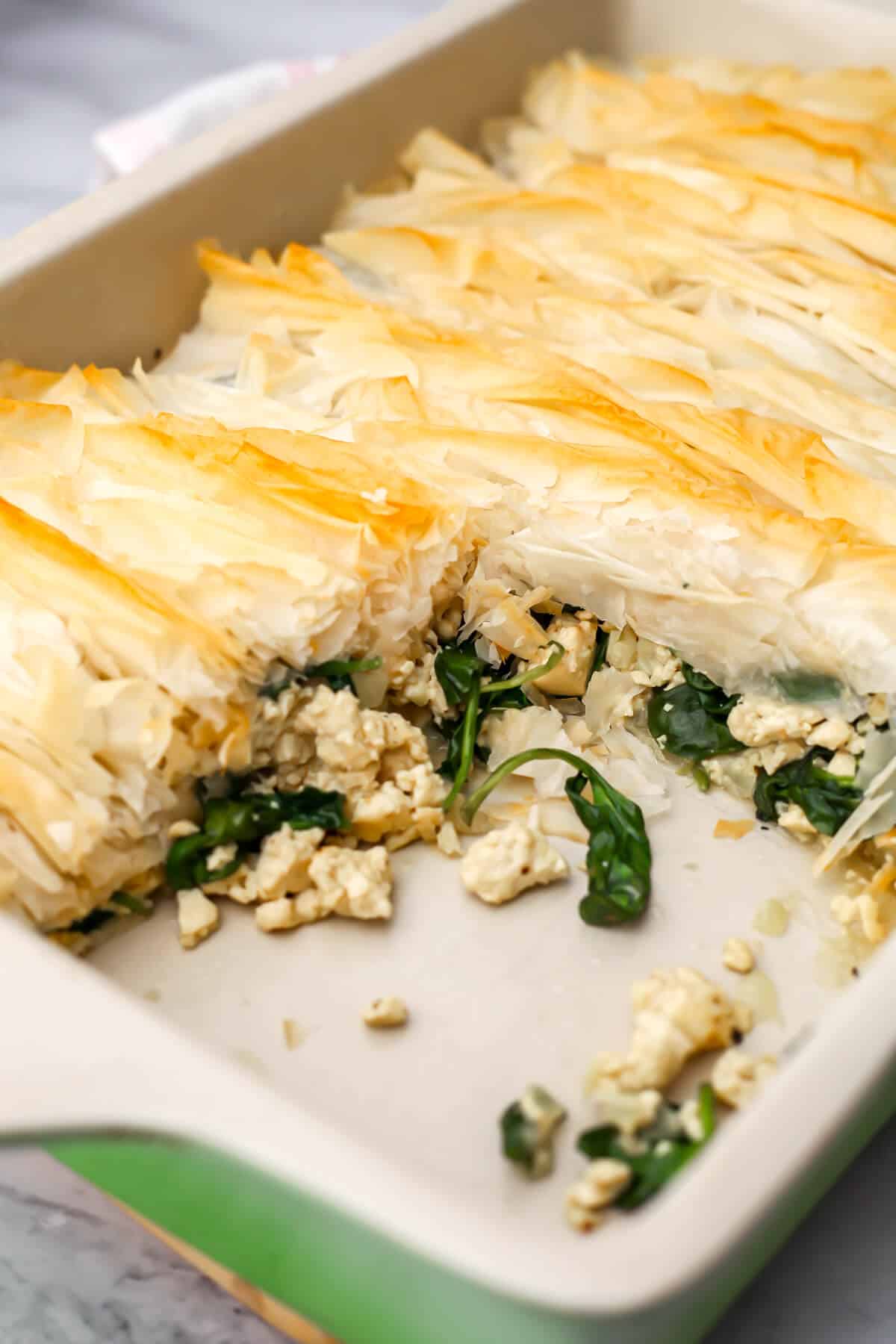A baking dish with tofu spanakopita topped with a crispy layer of filo.