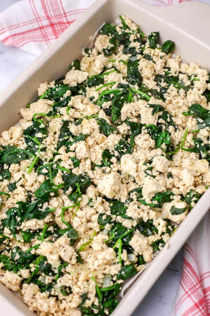 Tofu and spinach added to the bottom of a baking dish.