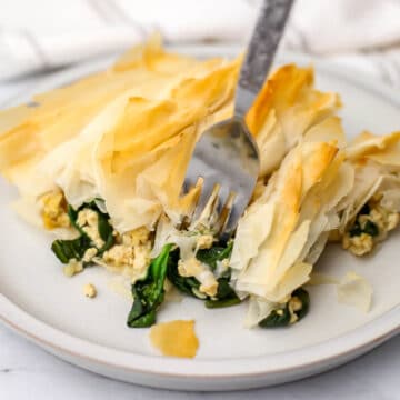 A piece of vegan Spanakopita made with tofu and filo with a fork in it.
