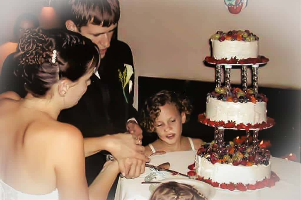 Bride and groom cutting into a wedding cake made of vegan carrot cake and topped with fruit.