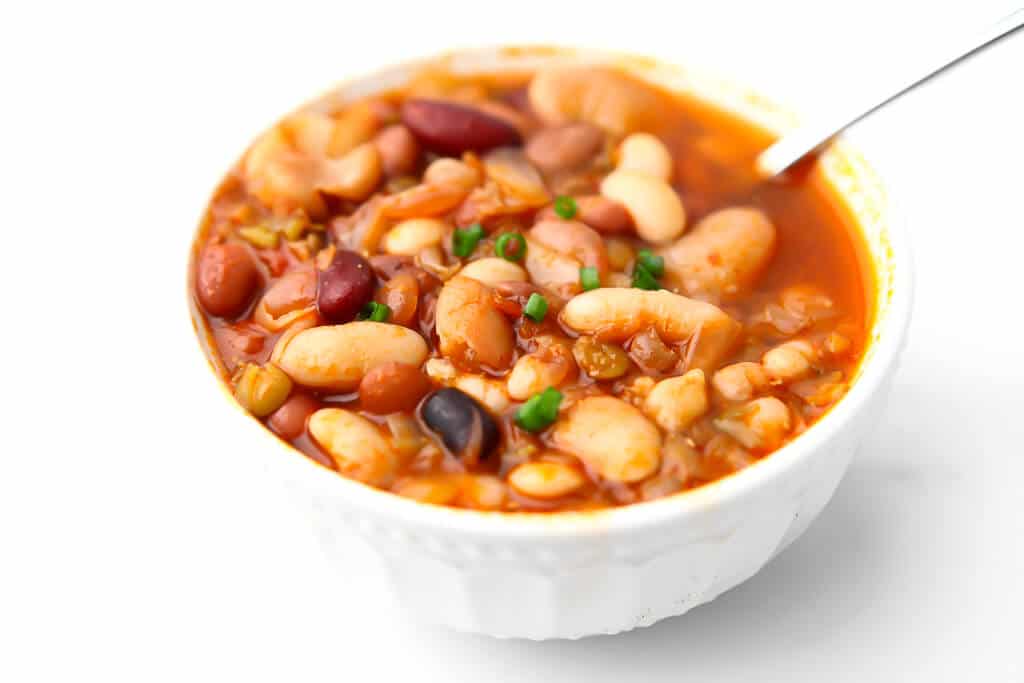 A white bowl filled with vegan 15 bean soup with a spoon in it.