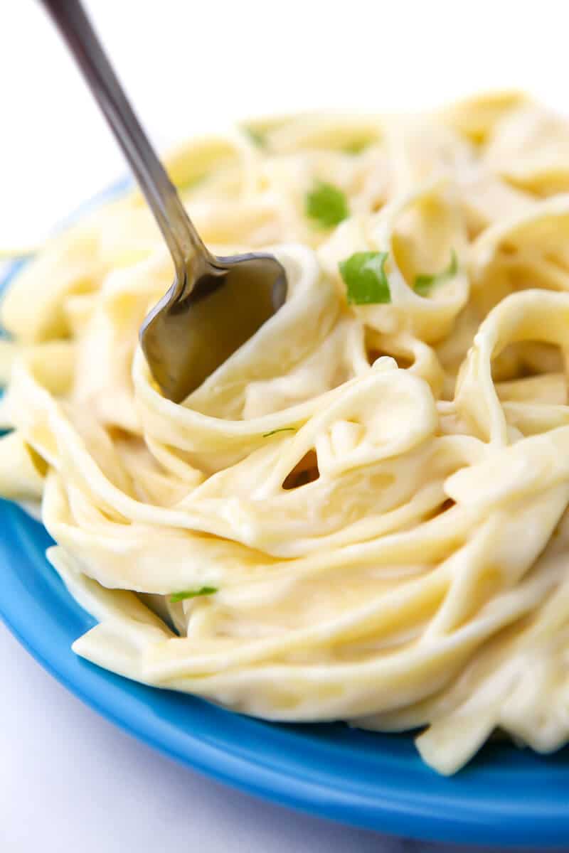 A blue plate full of vegan fettuccine Alfredo made with coconut milk.