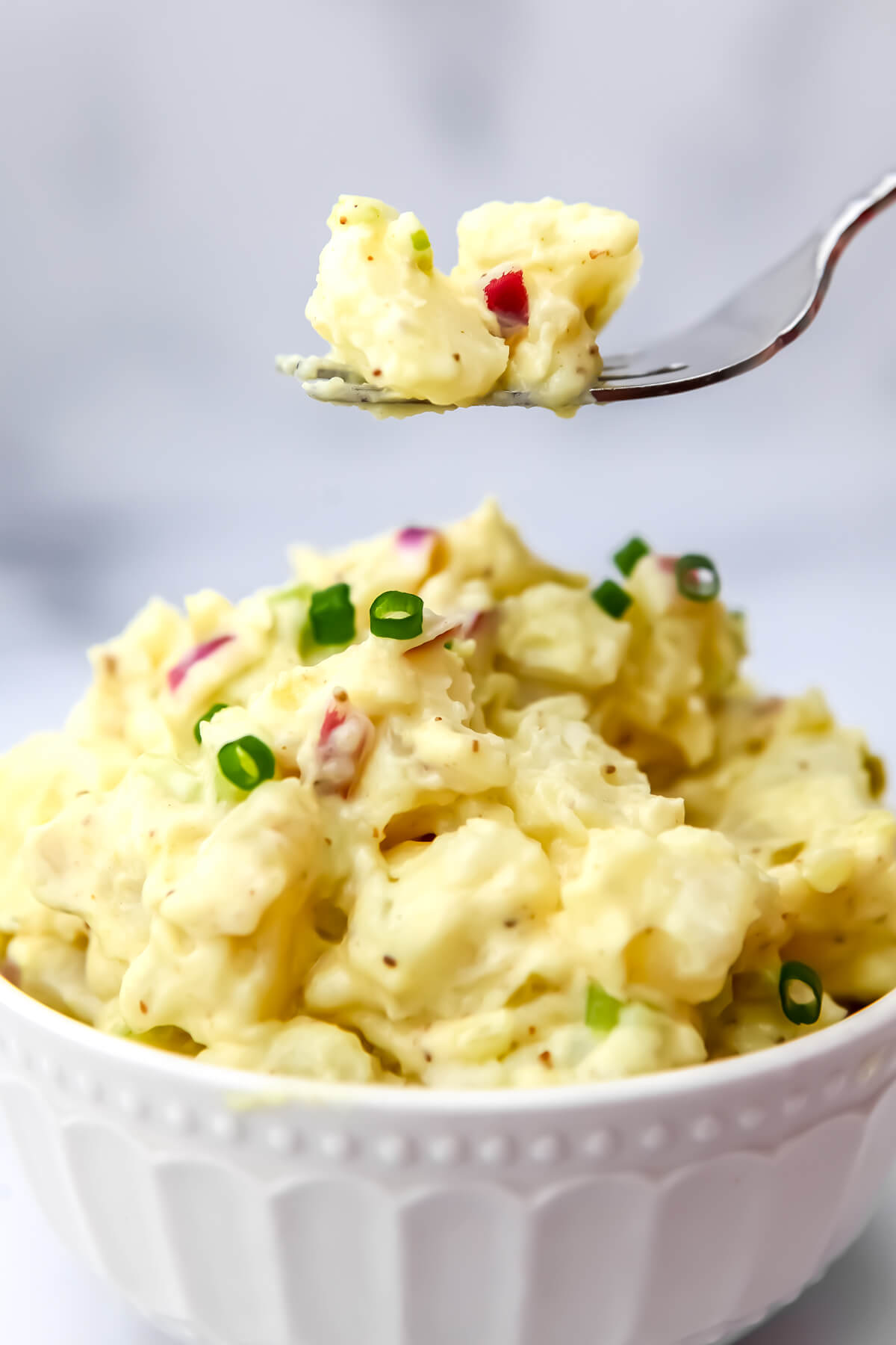 A white bowl filled with vegan potato salad with a fork full over it.