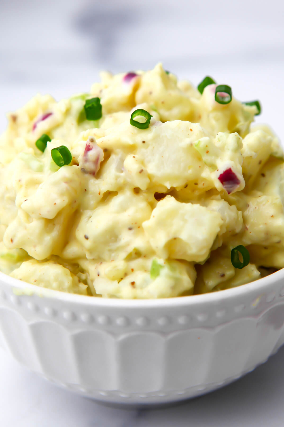 A heaping bowl of vegan potato salad with red onions mixed in and chives on top.