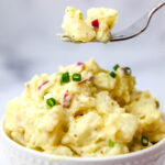 classic vegan potato salad with red onion and chives on top being scooped up with a fork.