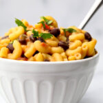 A white bowl filled with spicy southwest-style vegan mac and cheese with beans and corn.