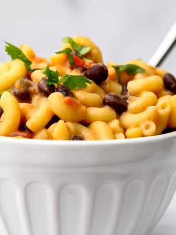 A white bowl filled with spicy southwest-style vegan mac and cheese with beans and corn.