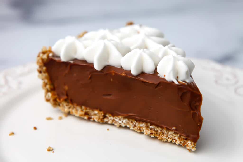 A slice of vegan chocolate pie on a white plate topped with vegan whipped cream.