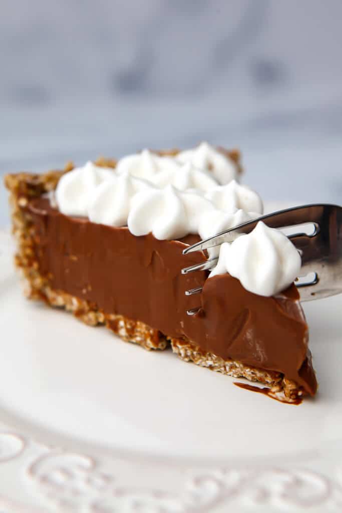 A slice of a vegan chocolate pie with vegan whipped cream on top with a fork cutting into it.