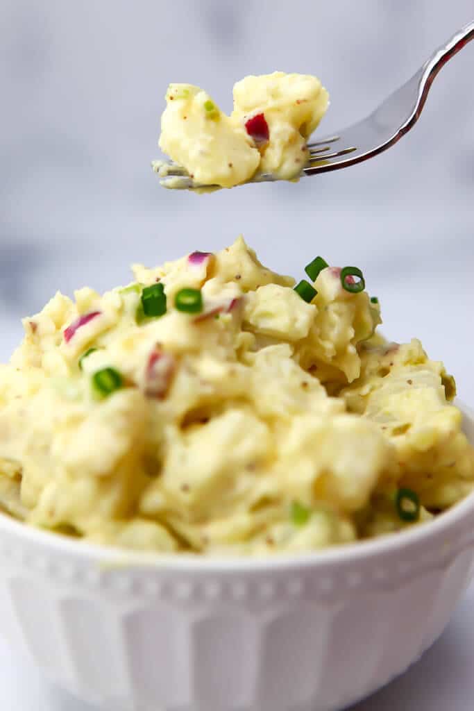 A white bowl filled with vegan potato salad with a fork full over it.
