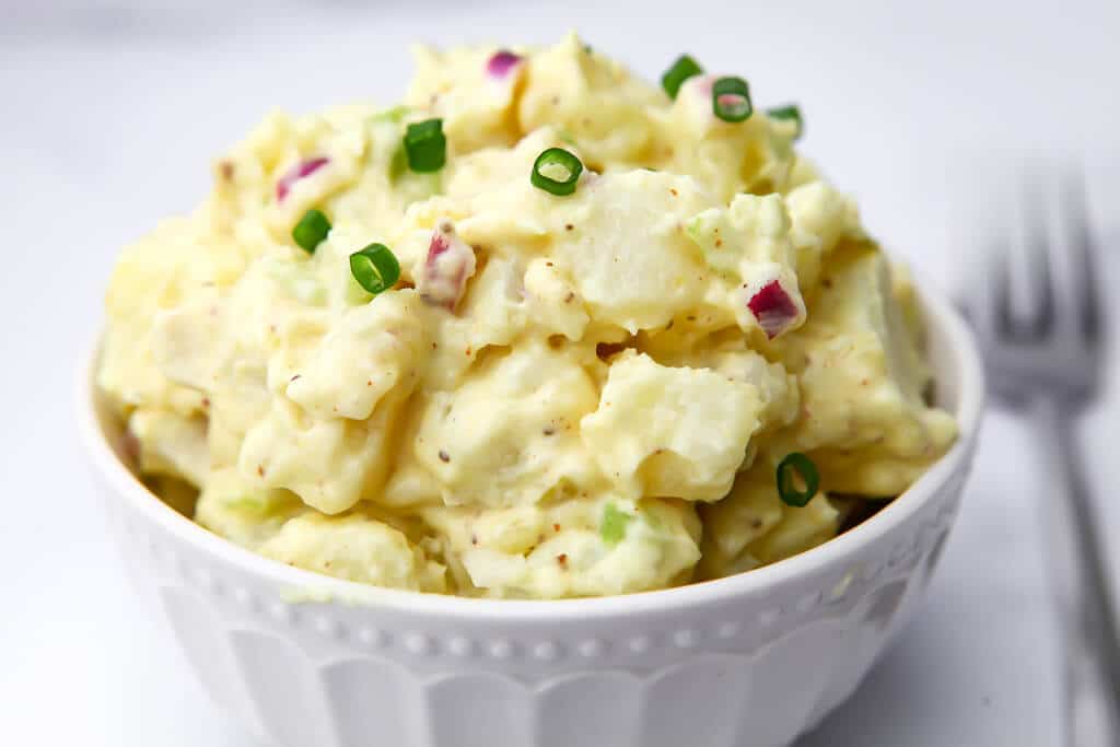 A close up of a vegan potato salad in a white bowl.