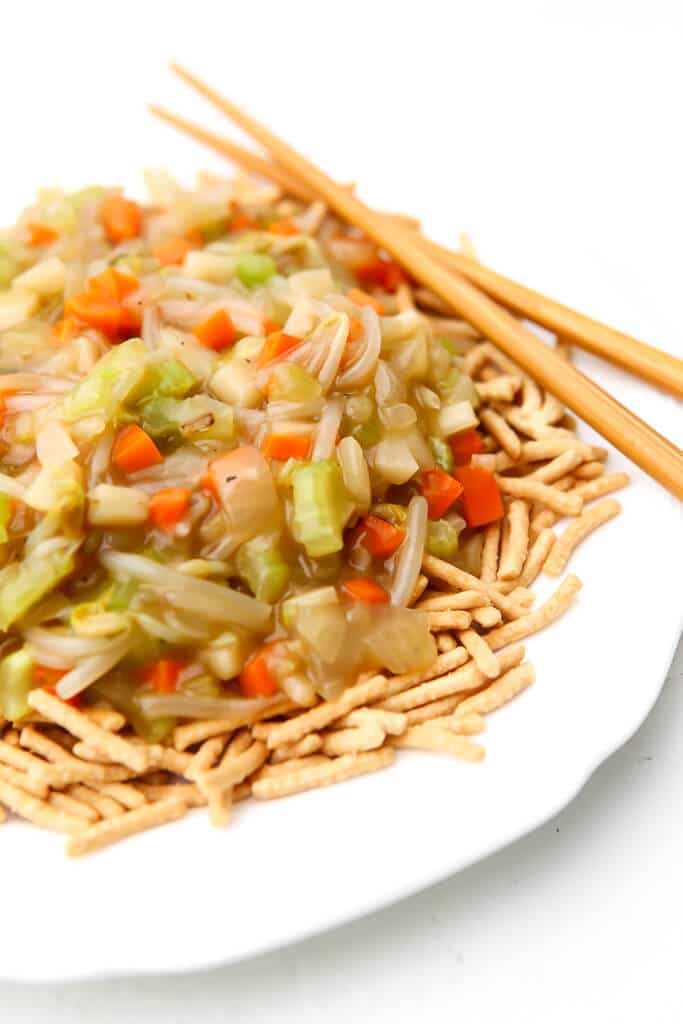 A white plate filled with chow mein noodles topped with vegetable chop suey.