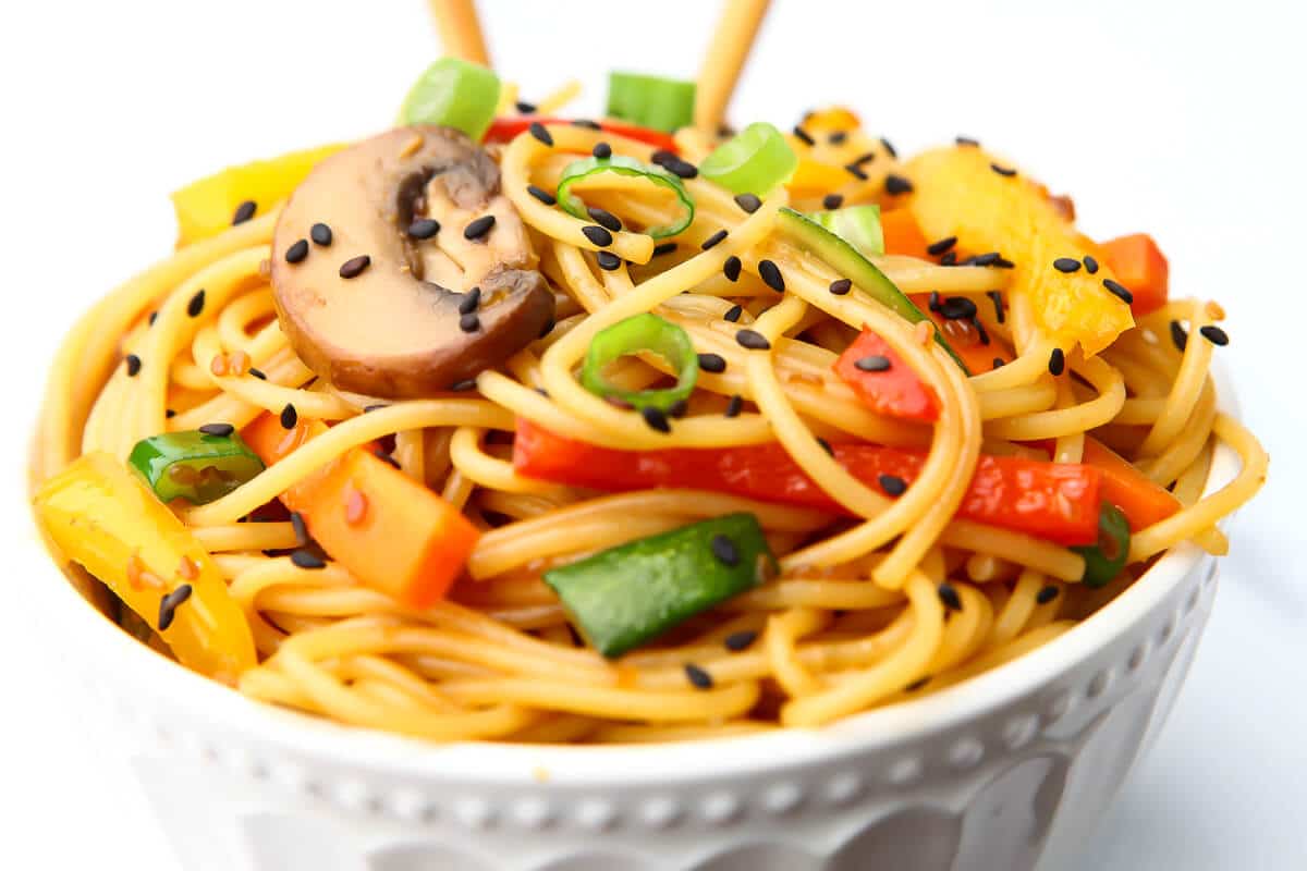 A bowl filled with noodles and sauteed veggies topped with teriyaki sauce and black sesame seeds.