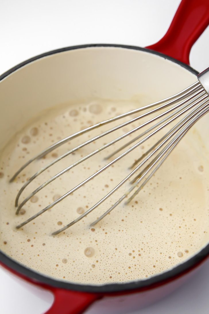 Vegan cheese sauce in a saucepan being stirred with a whisk.