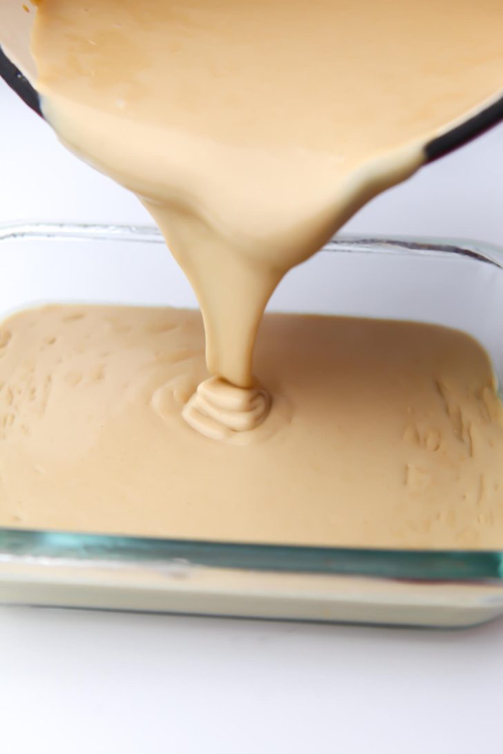Pouring the homemade vegan cheese into a glass cheese container.