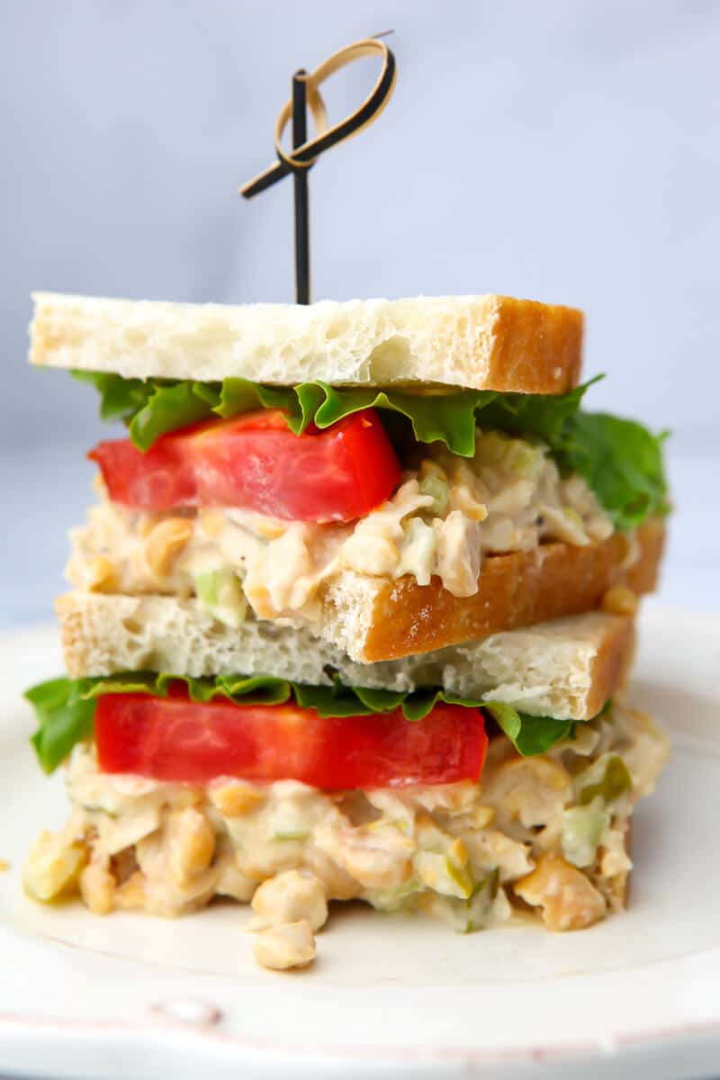 A vegan chickpea salad sandwich with lettuce and tomato cut in half and stacked on top of eachother.