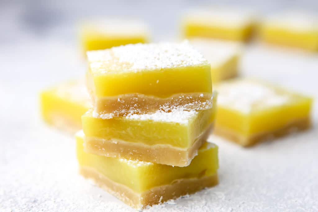 Three dairy-free lemon bars stacked up with some more behind them.