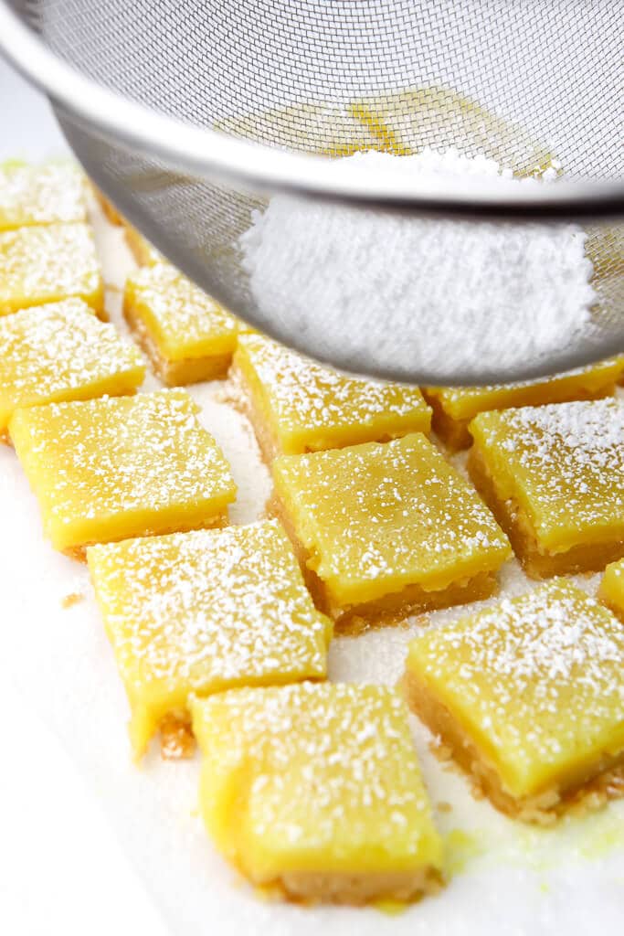 Dusting vegan lemon squares with powdered sugar using a wire mesh strainer.