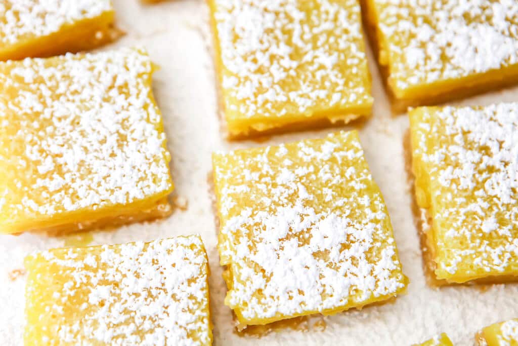 A top view of dairy-free lemon bars on parchment paper sprinkled with powdered sugar. 