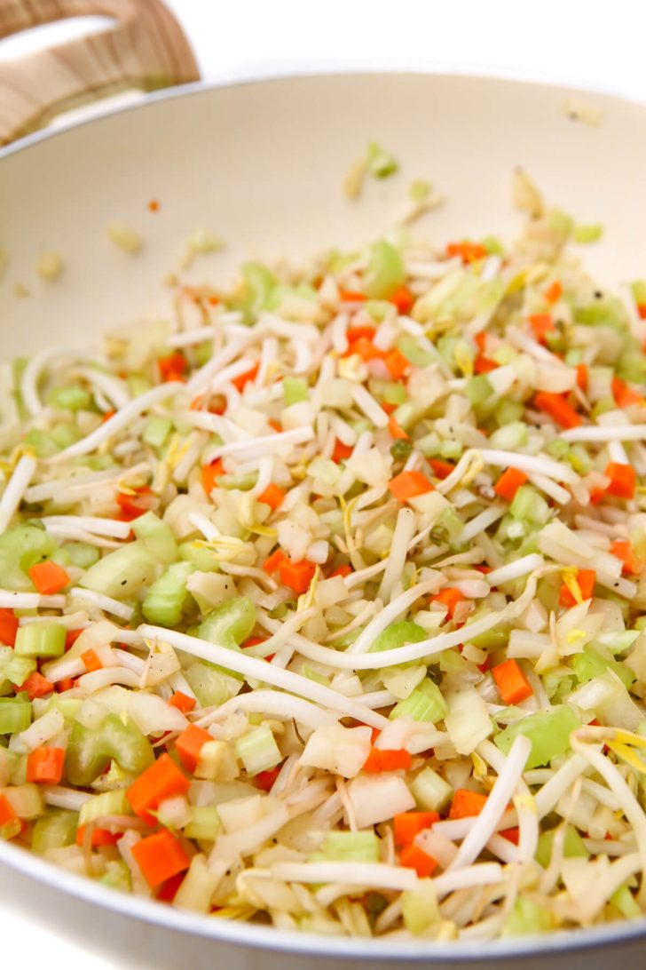 Onions, carrots, celery, and bean sprouts sautéing in a pan to make vegetable chop suey.