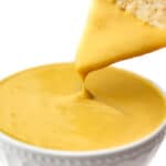 A vegan cheese sauce made from vegetables in a white bowl with a chip being dipped into it.