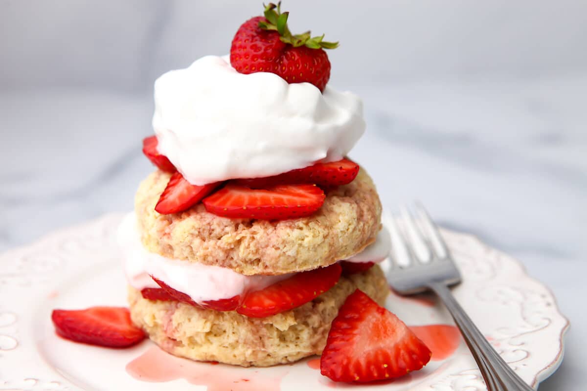 A vegan strawberry shortcake stacked on a white plate with layers of strawberries and vegan whipped cream.