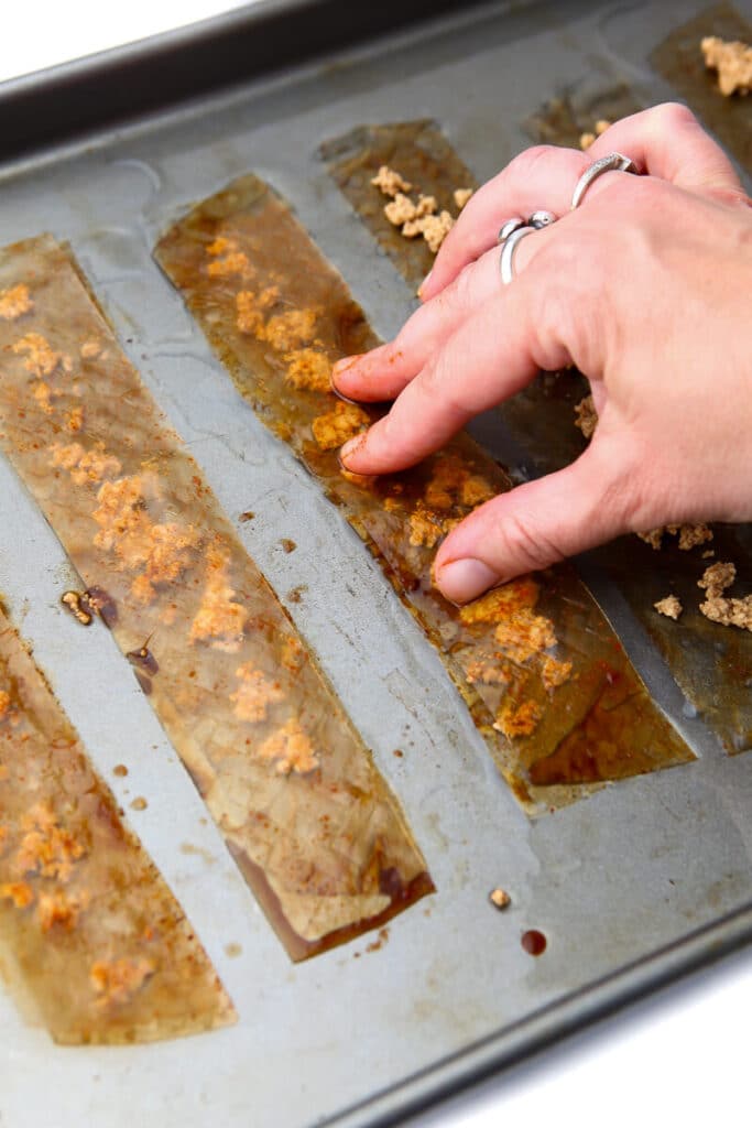 A hand putting the top layer of rice paper on the other rice paper and tofu layer to make vegan bacon.