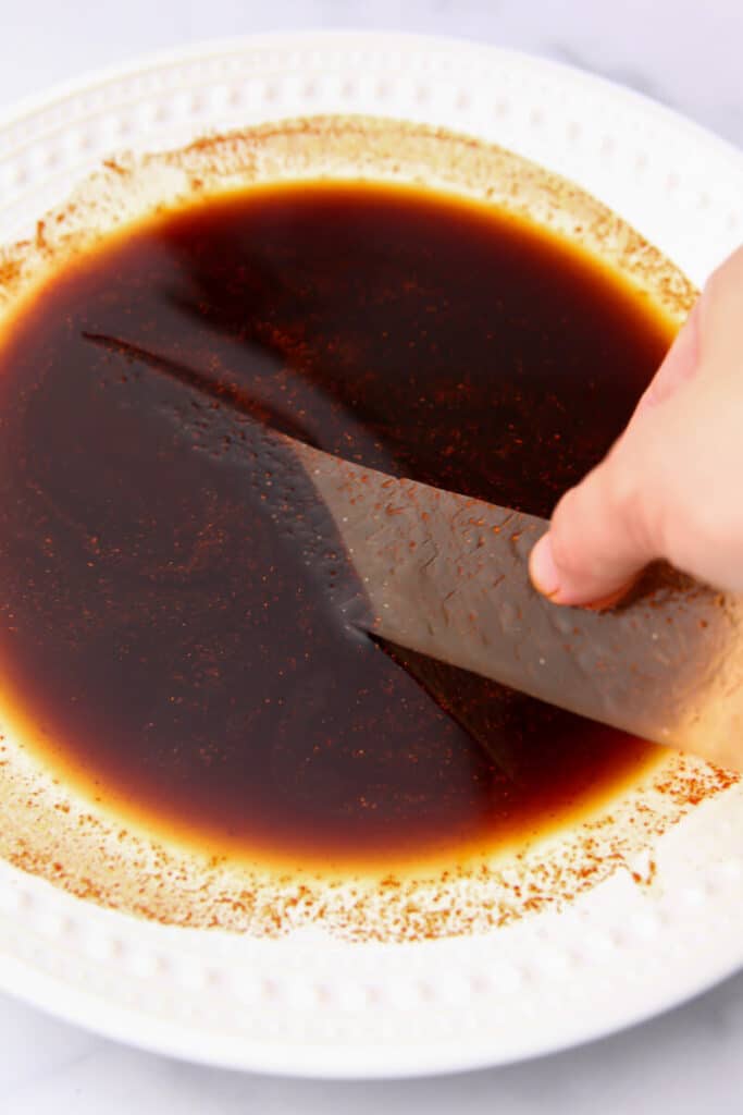 Rice paper being dipped into a bacon flavored marinade.