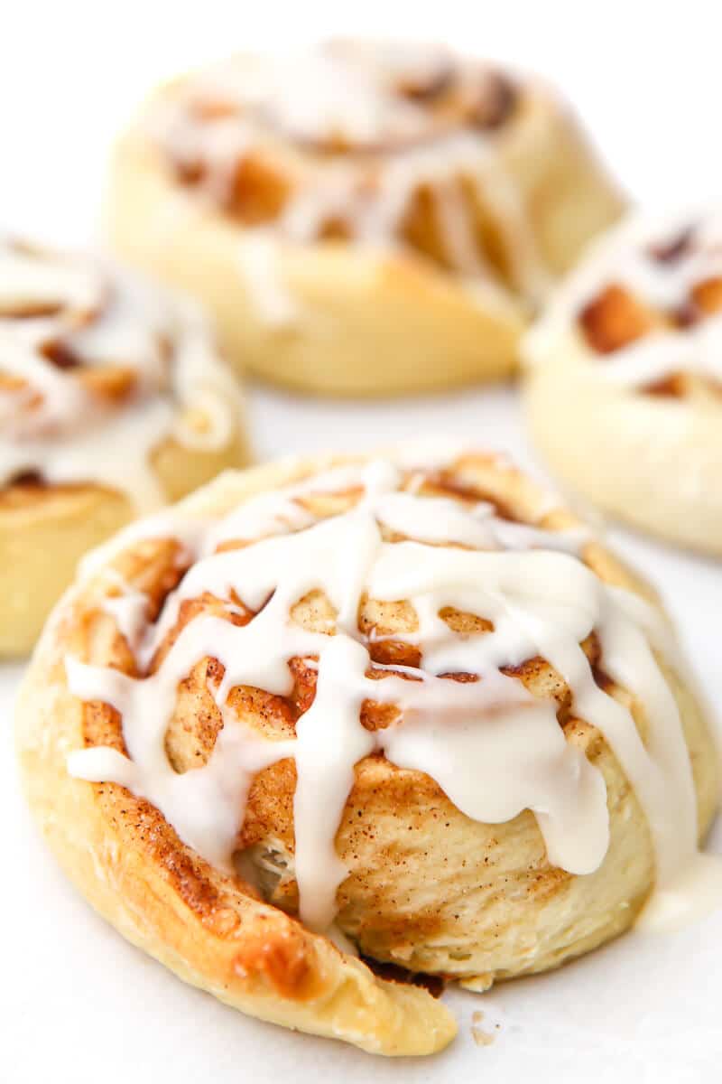 A close up of a vegan cinnamon roll with 3 others behind it on a white surface.
